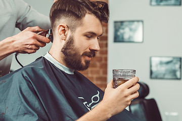 Image showing The hands of young barber making haircut to attractive man in barbershop