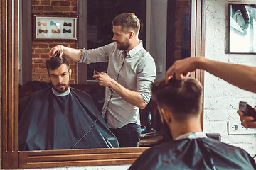 Image showing Young handsome barber making haircut of attractive man in barbershop