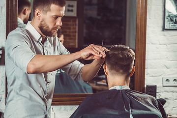 Image showing Young handsome barber making haircut of attractive man in barbershop