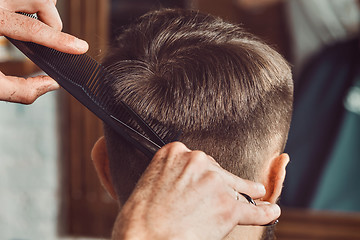 Image showing The hands of young barber making haircut to attractive man in barbershop