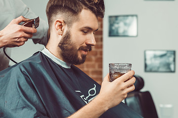 Image showing The hands of young barber making haircut to attractive man in barbershop