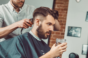 Image showing Young handsome barber making haircut of attractive man in barbershop