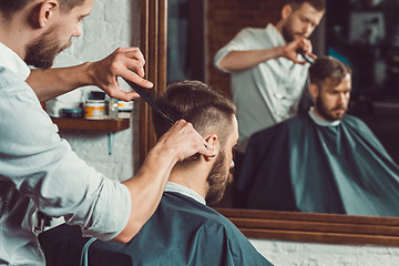 Image showing Young handsome barber making haircut of attractive man in barbershop