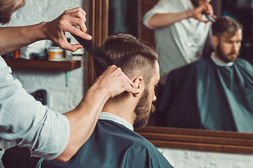 Image showing The hands of young barber making haircut to attractive man in barbershop