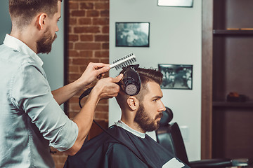 Image showing Young handsome barber making haircut of attractive man in barbershop