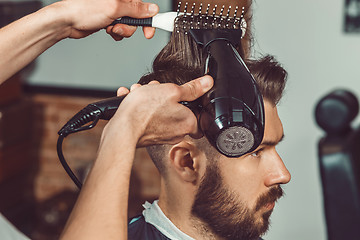 Image showing The hands of young barber making haircut to attractive man in barbershop