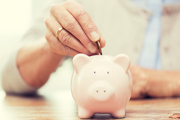 Image showing senior woman hand putting money to piggy bank