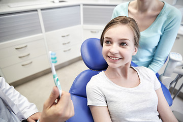 Image showing happy dentist showing toothbrush to patient girl