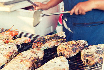 Image showing close up of cook hands grilling fish on street