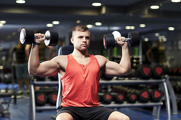 Image showing young man with dumbbells flexing muscles in gym