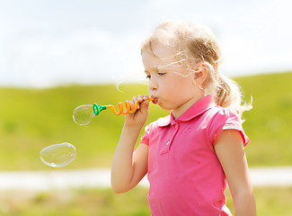 Image showing little girl blowing soap bubbles outdoors