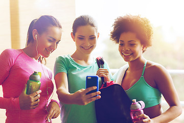 Image showing happy women with bottles and smartphone in gym