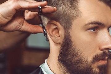 Image showing The hands of young barber making haircut to attractive man in barbershop