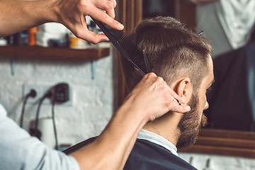 Image showing The hands of young barber making haircut to attractive man in barbershop