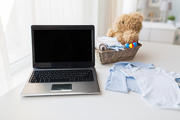 Image showing close up of baby clothes, toys and laptop at home