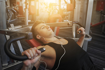 Image showing young man with earphones exercising on gym machine