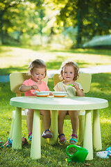 Image showing Two little girls sitting at a table and eating together against green lawn