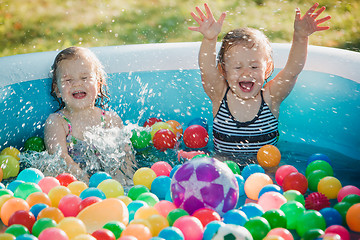 Image showing The two little baby girls playing with toys in inflatable pool in the summer sunny day