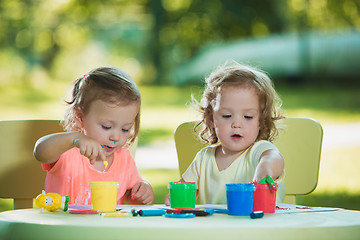 Image showing Two-year old girls painting with poster paintings together against green lawn