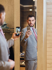 Image showing man in suit taking mirror selfie at clothing store