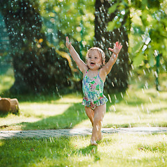 Image showing The little baby girl playing with garden sprinkler.