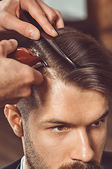 Image showing The hands of young barber making haircut to attractive man in barbershop