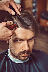 Image showing The hands of young barber making haircut to attractive man in barbershop