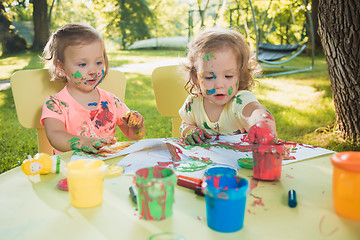 Image showing Two-year old girls painting with poster paintings together against green lawn