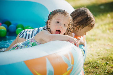 Image showing The two little baby girls playing with toys in inflatable pool in the summer sunny day