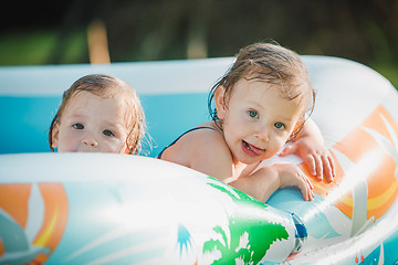 Image showing The two little baby girls playing with toys in inflatable pool in the summer sunny day