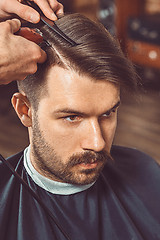 Image showing The hands of young barber making haircut to attractive man in barbershop