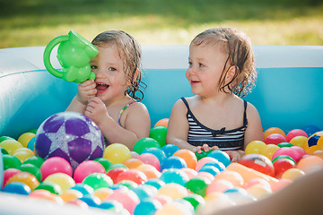 Image showing The two little baby girls playing with toys in inflatable pool in the summer sunny day