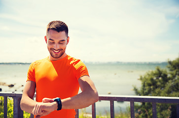 Image showing smiling young man with smart wristwatch at seaside