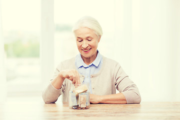 Image showing senior woman putting money into glass jar at home