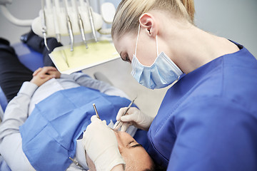 Image showing female dentist in mask checking male patient teeth