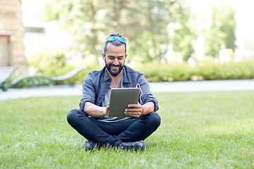 Image showing man with earphones and tablet pc sitting on grass