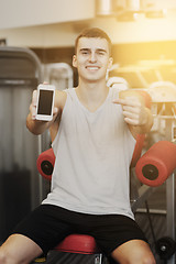 Image showing smiling young man with smartphone in gym