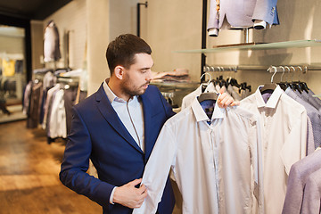 Image showing happy young man choosing shirt in clothing store