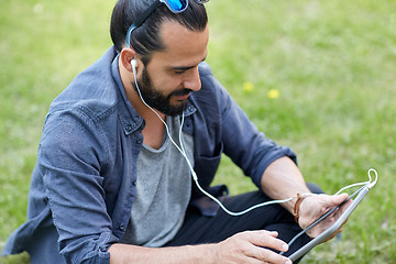 Image showing man with earphones and tablet pc sitting on grass