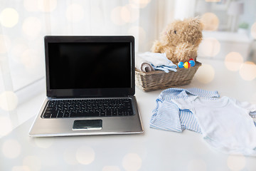 Image showing close up of baby clothes, toys and laptop at home