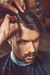 Image showing The hands of young barber making haircut to attractive man in barbershop