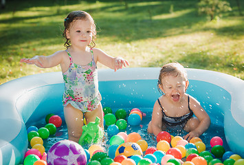 Image showing The two little baby girls playing with toys in inflatable pool in the summer sunny day