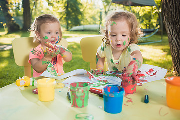 Image showing Two-year old girls painting with poster paintings together against green lawn