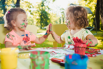 Image showing Two-year old girls painting with poster paintings together against green lawn