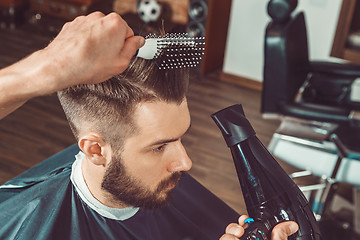 Image showing The hands of young barber making haircut to attractive man in barbershop