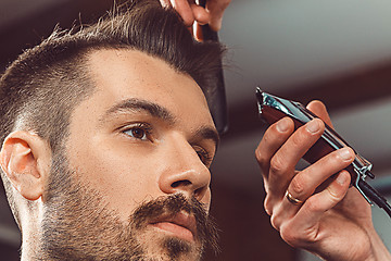 Image showing The hands of young barber making haircut to attractive man in barbershop