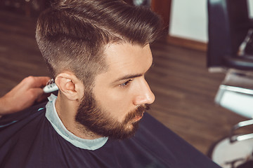 Image showing The hands of young barber making haircut to attractive man in barbershop