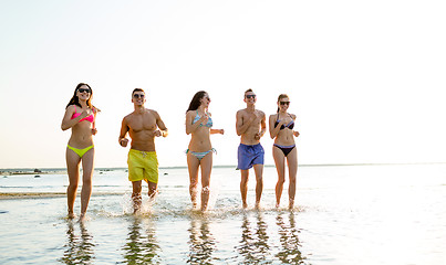 Image showing smiling friends in sunglasses running on beach