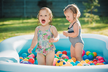 Image showing The two little baby girls playing with toys in inflatable pool in the summer sunny day