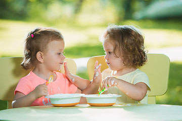 Image showing Two little girls sitting at a table and eating together against green lawn